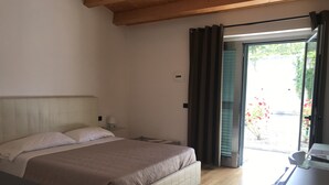 A bedroom with a bed, bedside table, and a view of a garden through a door. - Oasi del Vetoio (L'Aquila)