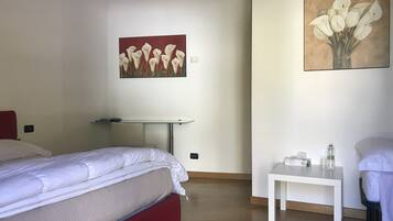 Habitación de hotel con dos camas, una mesita y dos cuadros en las paredes.