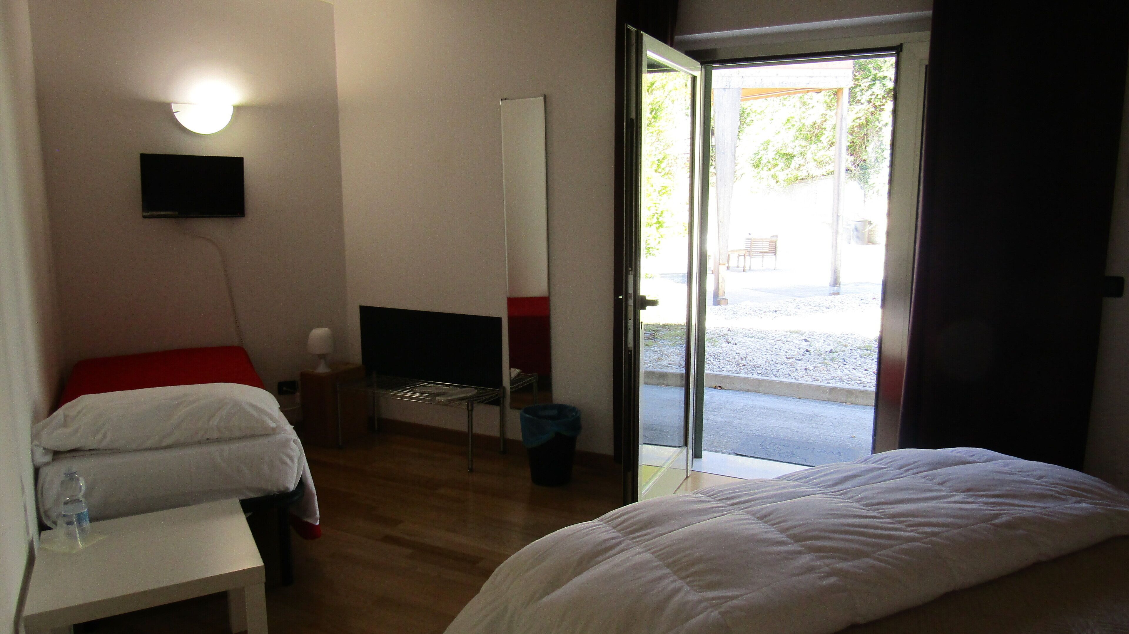 A hotel room with a bed, a desk, a TV, and a door leading to an outdoor area.