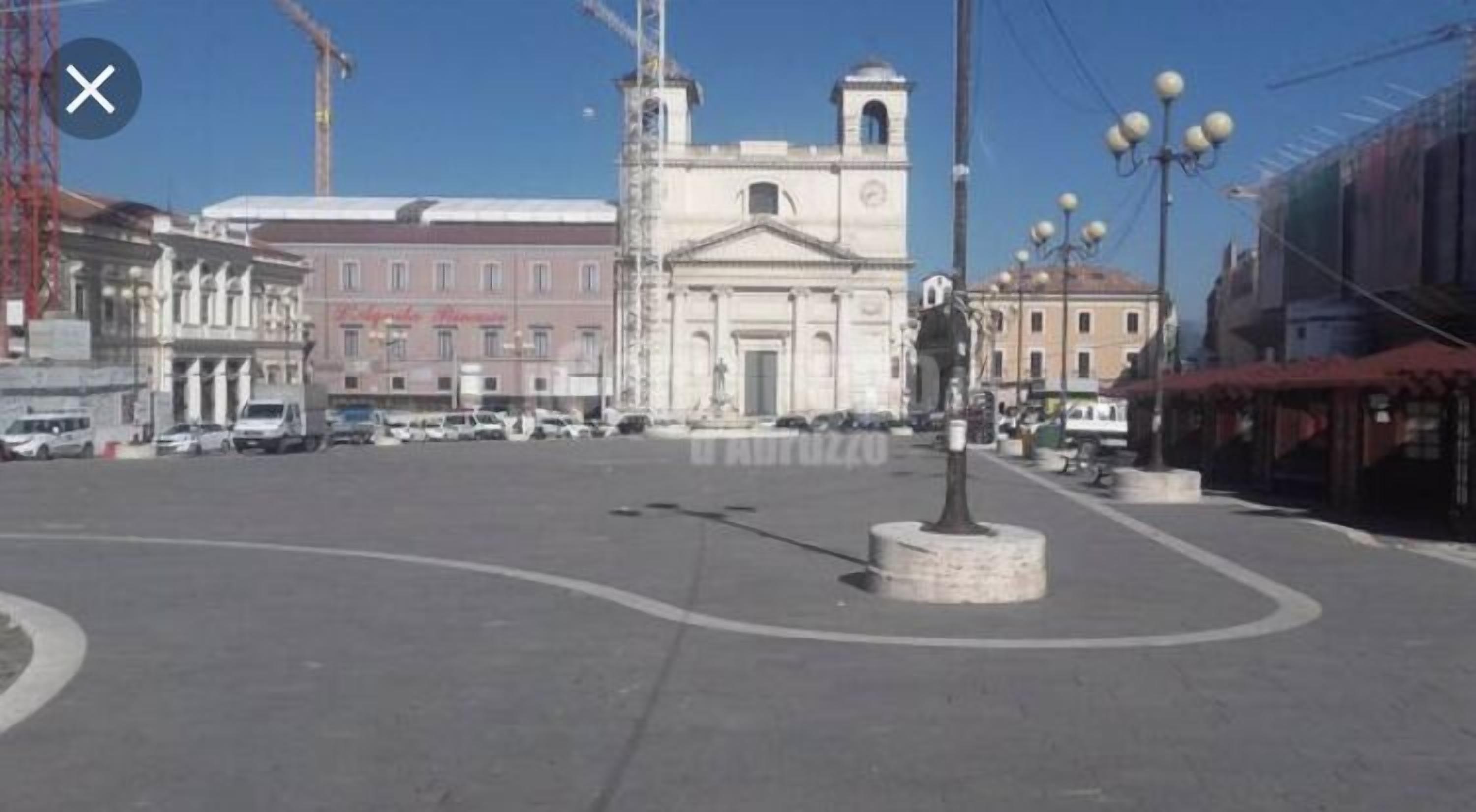 A public square with a central monument, surrounding buildings, and a clear sky.