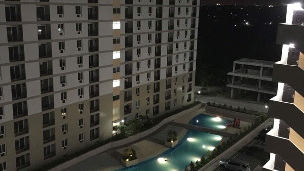 Un hotel alt amb diverses plantes, una piscina i una zona d'aparcament.