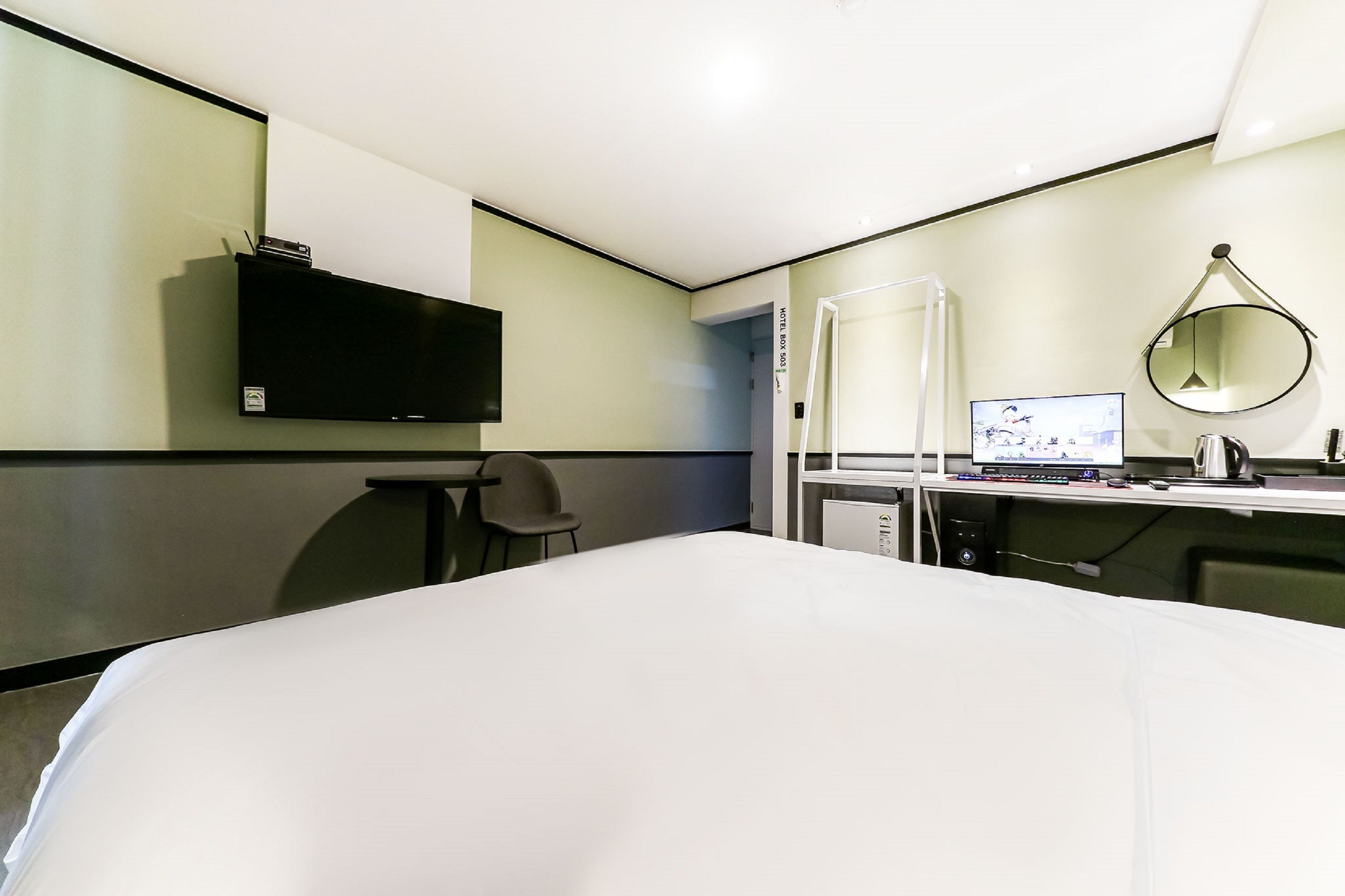 Habitación de hotel con cama, escritorio, computadora, silla, televisor y espejo.
