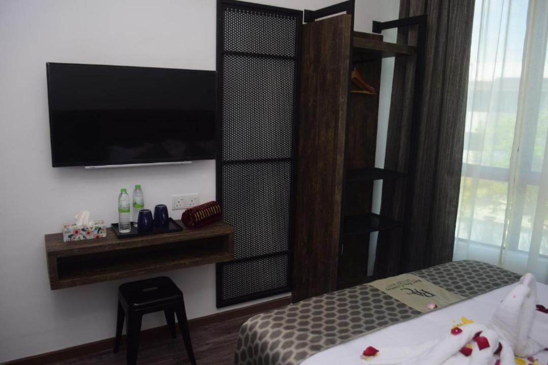 Habitación de hotel con cama, televisión montada en la pared, escritorio pequeño con artículos de aseo y ventana con cortinas.