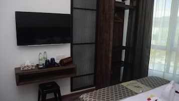 Habitación de hotel con cama, televisión montada en la pared, escritorio pequeño con artículos de aseo y ventana con cortinas.