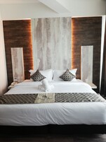 Una habitación de hotel con una cama grande, ropa de cama blanca, almohadas estampadas y un teléfono en la mesita de noche.