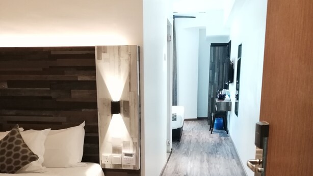 A hotel room with a wooden headboard, a bedside table with a lamp, a bed with white bedding, and a wooden floor. - Rest and Comfort Boutique Hotel (Kuala Terengganu)