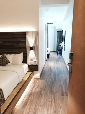 A hotel room with a wooden headboard, a bedside table with a lamp, a bed with white bedding, and a wooden floor. - Rest and Comfort Boutique Hotel (Kuala Terengganu)