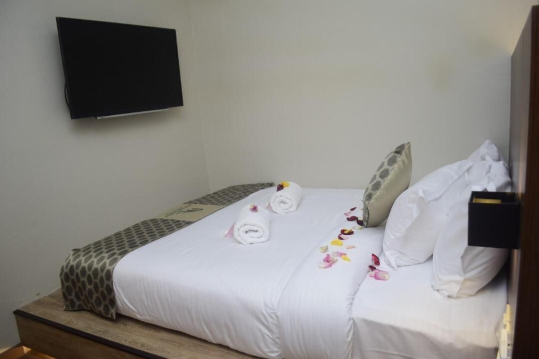 A neatly made bed with white linens, two rolled towels, and decorative flower petals.