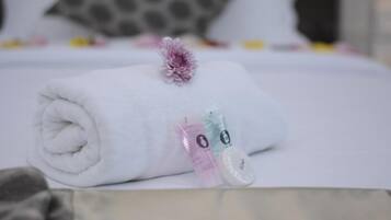 Una toalla blanca enrollada cuidadosamente, una flor morada, un cinta métrica y un pequeño recipiente con jabón sobre una cama.