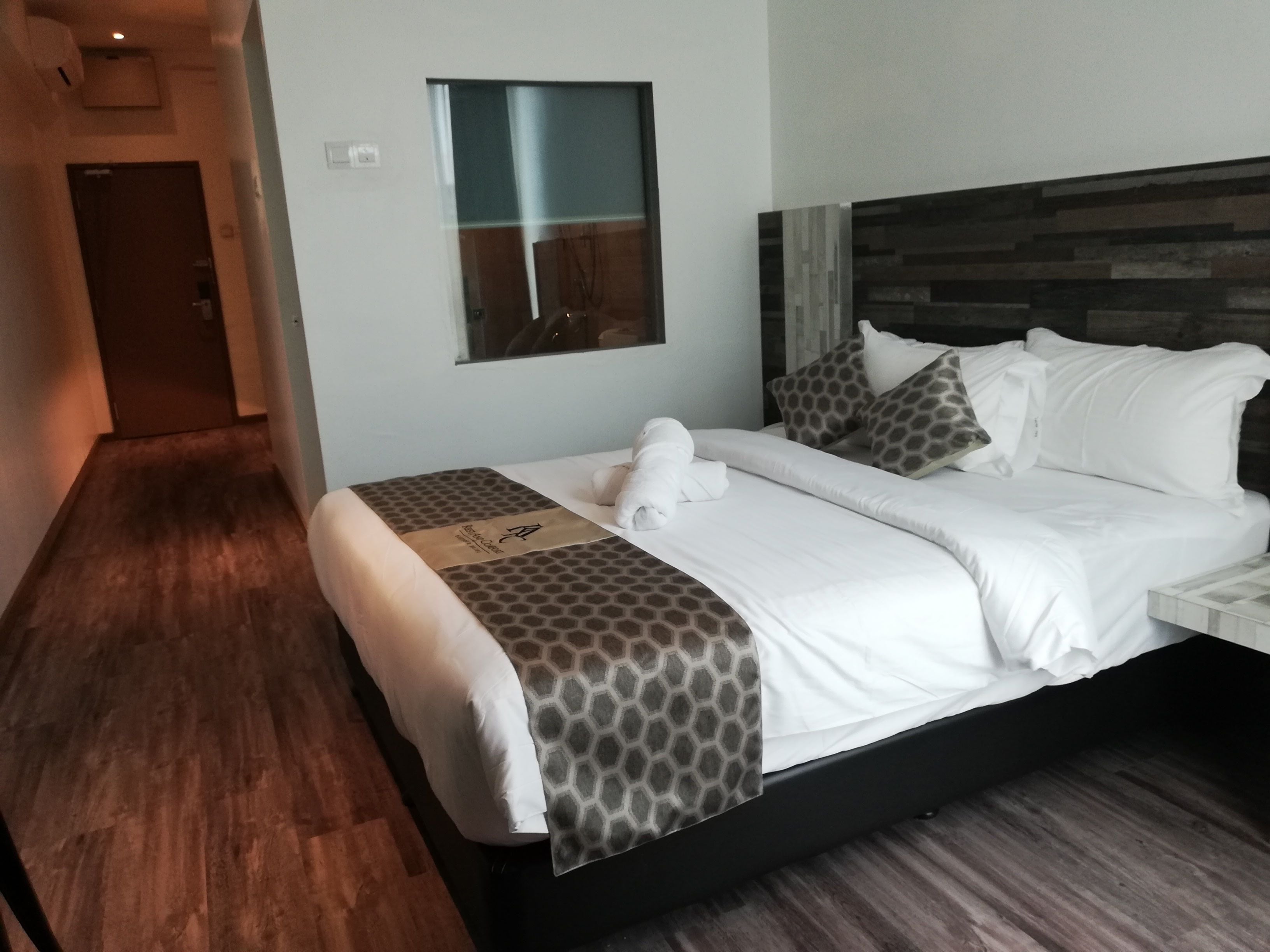 Een hotelkamer met een bed, een houten vloer, een raam en een deur.