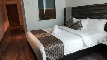 A hotel room with a bed, a wooden floor, a window, and a door.
