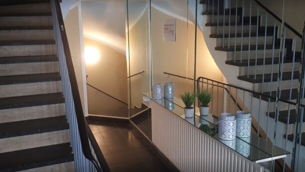 En trappe med glasgelændere og moderne design, der fører op til et platformsområde med dekorative vaser og en lille plante.