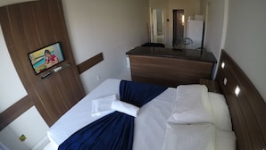A hotel room with a bed, a desk, a chair, a TV, and a mirror. - Residencial Ilhas Gregas (Florianópolis)