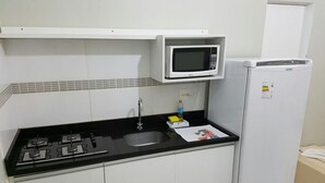 A compact kitchen with a gas stove, a microwave, and a refrigerator. - Residencial Ilhas Gregas (Florianópolis)
