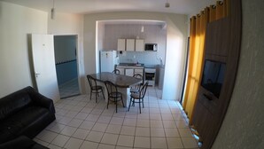 A compact living space with a dining area, kitchen, and a TV mounted on a wooden panel. - Residencial Ilhas Gregas (Florianópolis)