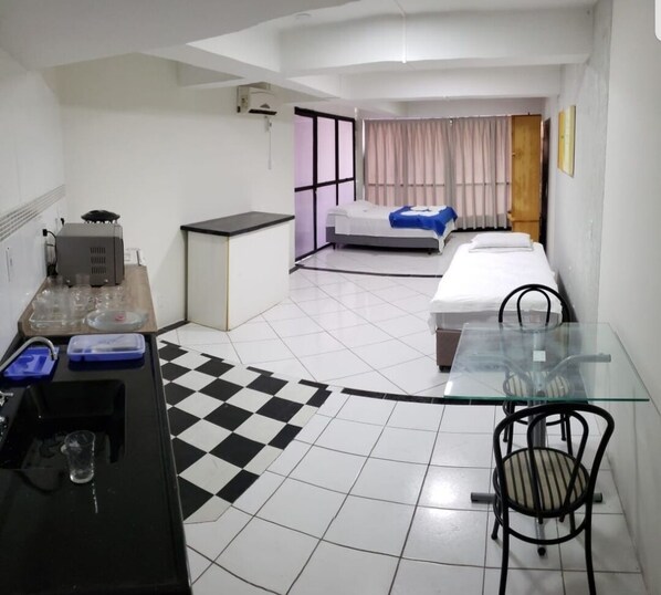 A compact hotel room with a kitchenette, a bed, a small table with chairs, and a checkered floor.