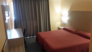 A hotel room with a bed, a desk, and a chair. There is a window with curtains, a nightstand with a lamp, and a wall-mounted light. - Mont-Park Hotel (Benidorm)