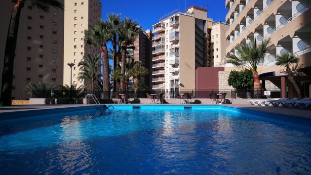 A swimming pool with lounge chairs and palm trees, surrounded by high-rise buildings. - Mont-Park Hotel (Benidorm)