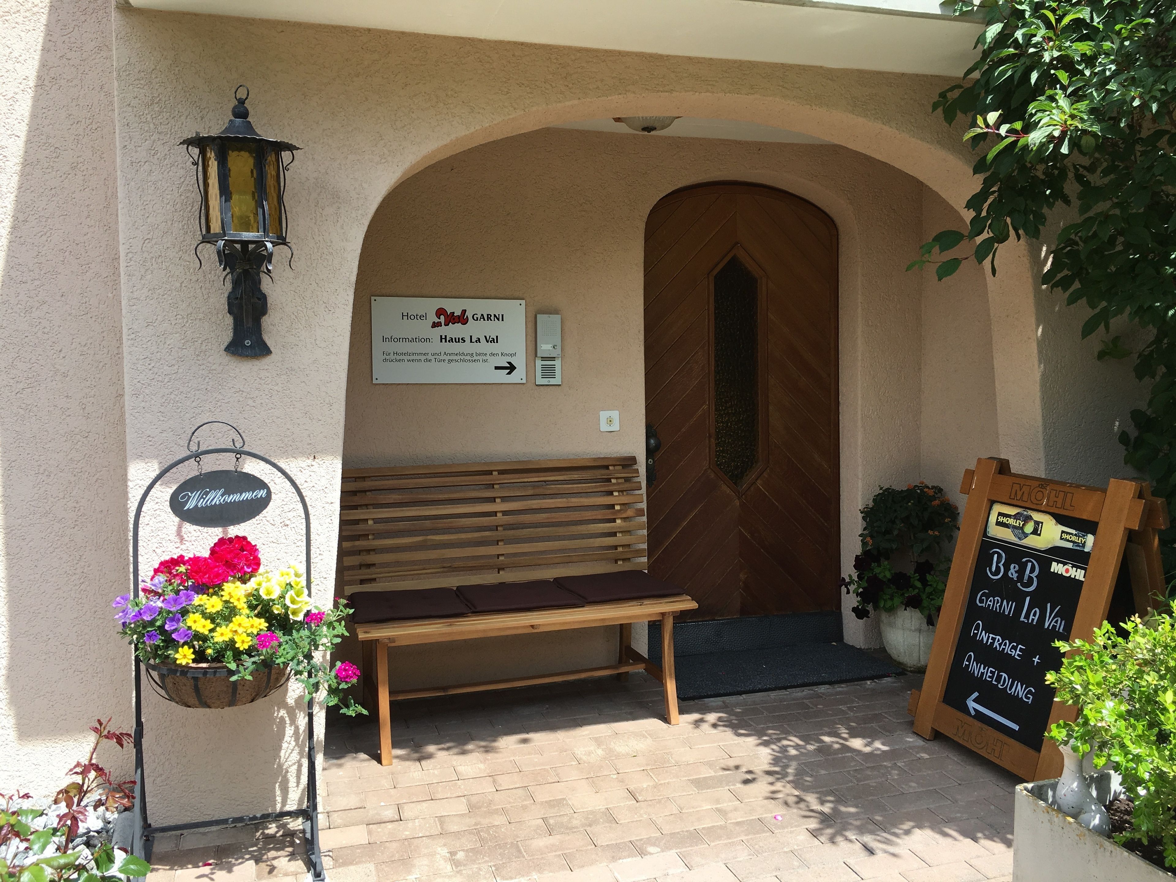 Entrada de hotel con un banco de madera, un letrero de bienvenida, una cesta de flores y una pizarra.