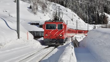 Un tren rojo sobre una vía cubierta de nieve, con montañas al fondo.