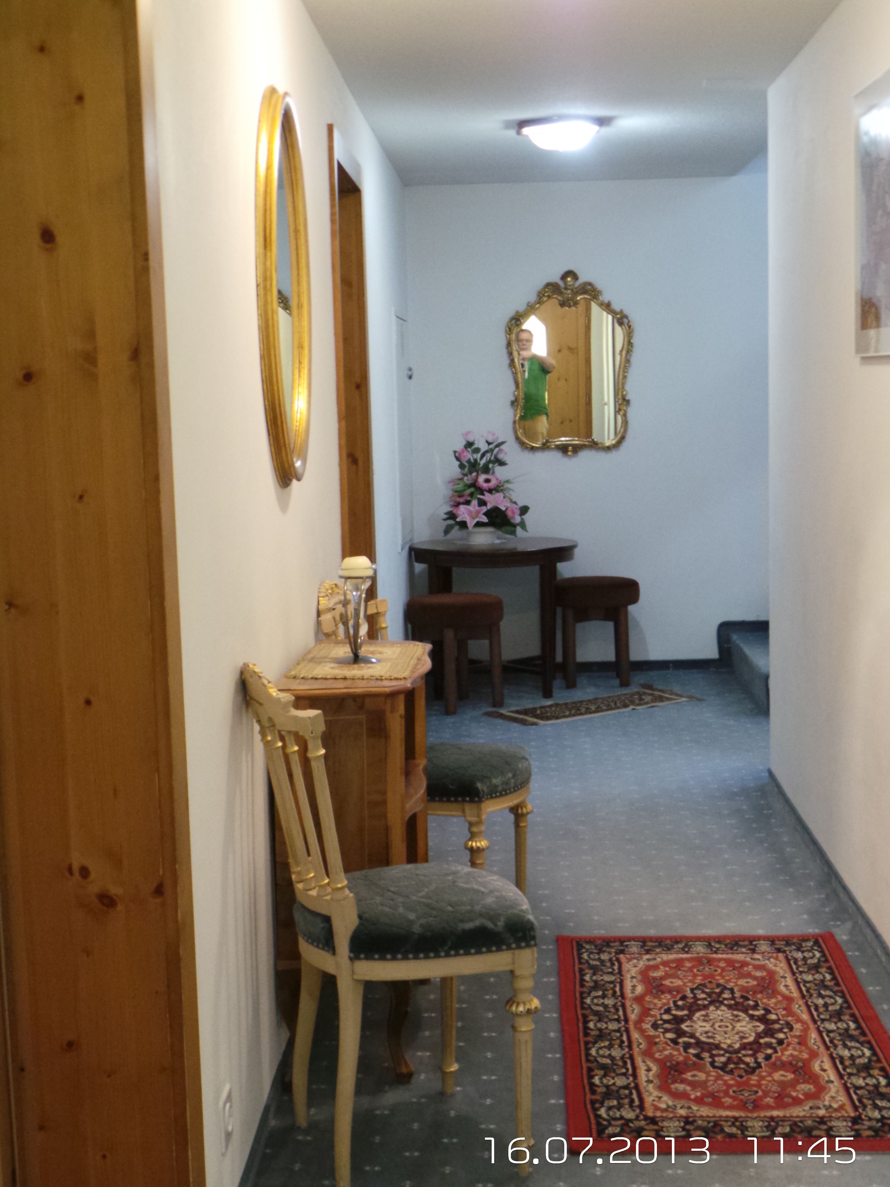 A hallway with a wooden door, a mirror, a small table with a vase of flowers, and a chair.