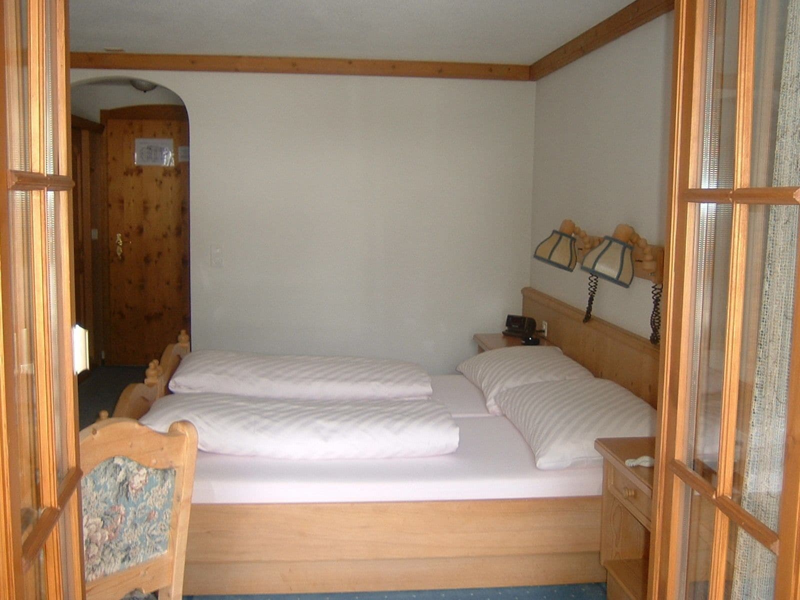Ein Schlafzimmer mit zwei Einzelbetten, Holz-Kopfteilen, einem Nachttisch mit Lampe und einer Holztür im Hintergrund.