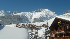 A mountain lodge with snow-covered roofs and a clear view of snow-capped peaks in the background. - B&B Garni Casa La Val (Tujetsch)
