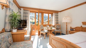 A hotel room with a bed, a desk with a TV, a chair, a table, and a potted plant. - B&B Garni Casa La Val (Tujetsch)