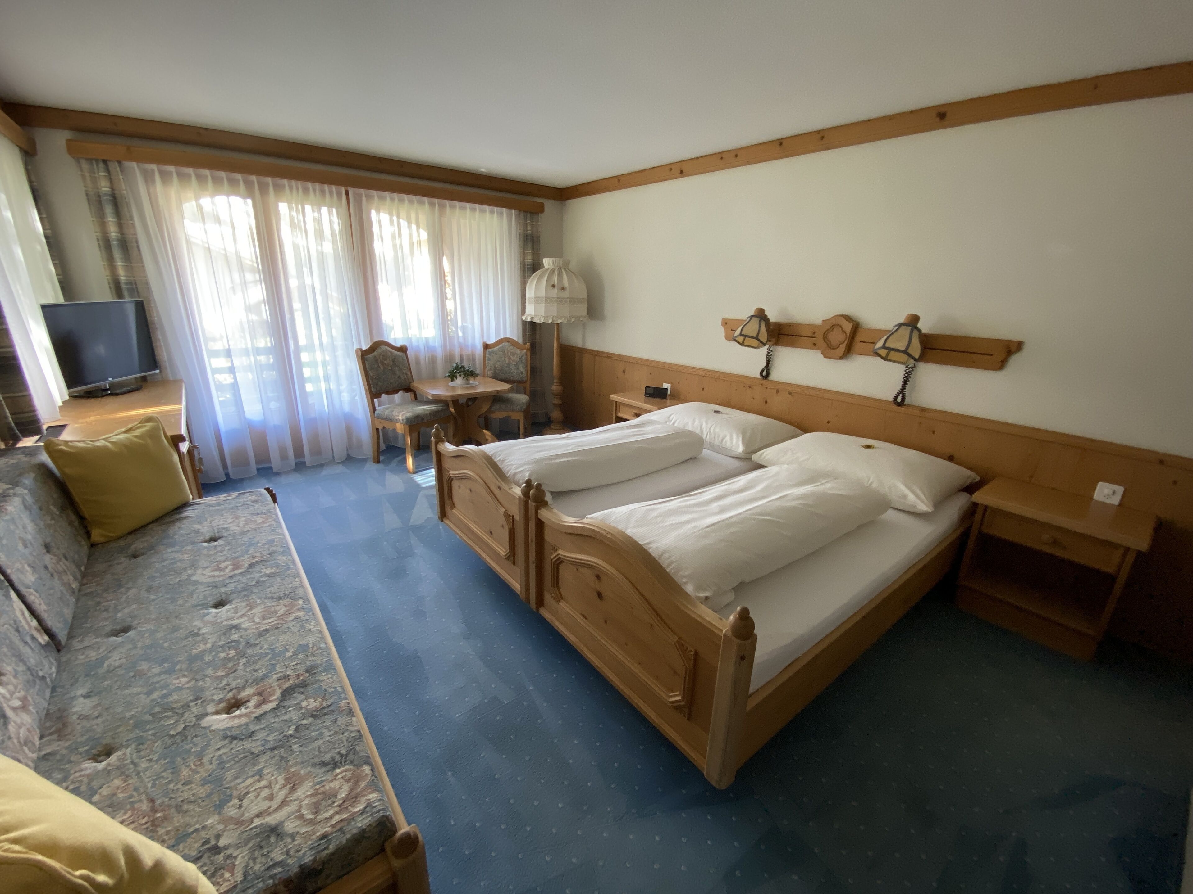 Habitación de hotel con cama doble, sofá, mesita, silla, televisión y lámpara.