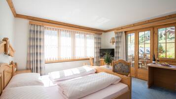 A bedroom with a bed, a desk, a TV, and a window with curtains.