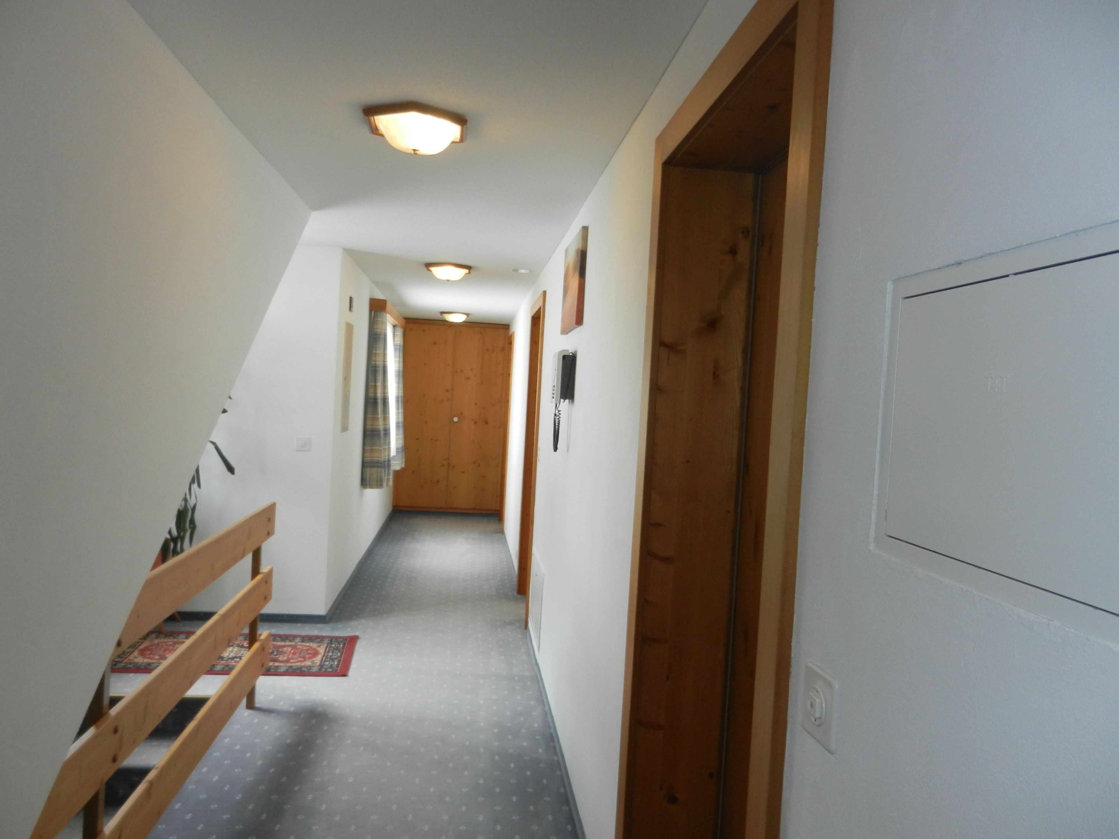 A narrow hallway with wooden doors, a bench, and a patterned rug.