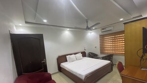 Un dormitorio con cama, una silla roja, escritorio, ventilador de techo y ventana con persianas.