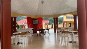 Un espacio de estar al aire libre cubierto con mesas y sillas, una pantalla de televisión y vistas de edificios al fondo.