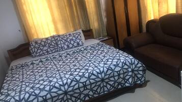 Una cama bien hecha con una colcha de estampado geométrico, un sillón de cuero marrón y una mesita de noche de madera con una lámpara.