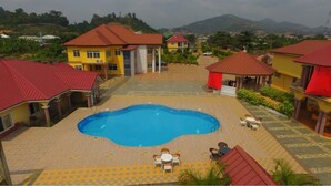 Un área de piscina con una piscina azul, rodeada de edificios amarillos con tejados rojos, y mobiliario de exterior.