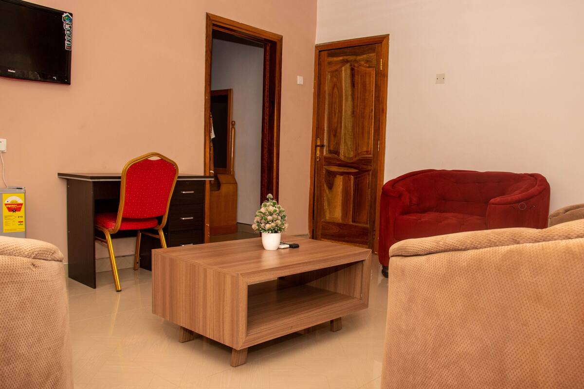 A living room with a wooden coffee table, a red chair, a red sofa, and a TV mounted on the wall.