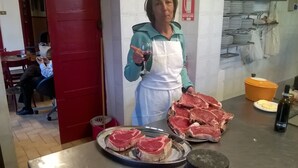 A person holding a glass of wine in a kitchen with raw meat on the counter. - Osteria Gaute La Nata (Viu)