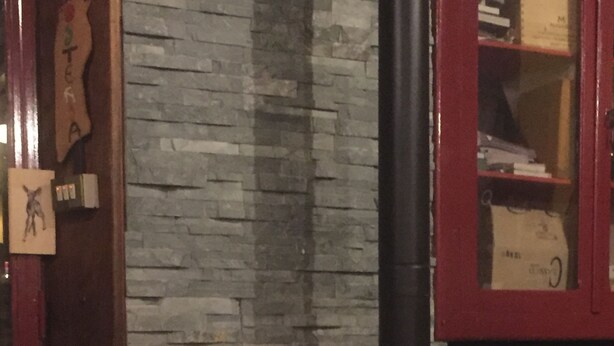A wood-burning stove with a visible fire, set against a stone wall and wooden door. - Osteria Gaute La Nata (Viu)