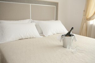 Un letto con biancheria bianca, un secchio con una bottiglia e dei bicchieri, e una testiera.