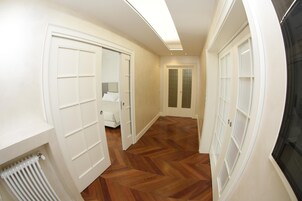 Un corridoio con pavimento in legno, porte bianche e un termosifone.