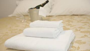 A neatly made bed with folded white towels and a bottle of champagne in a glass.