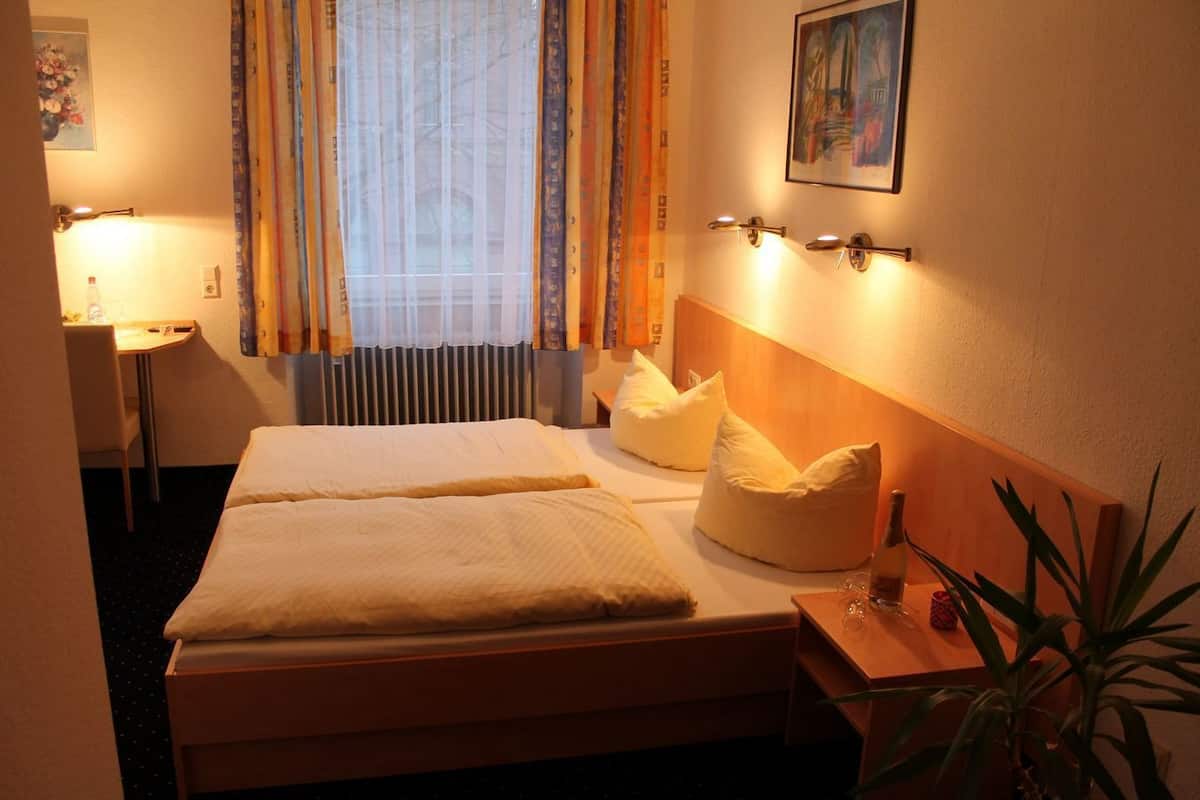 Een hotelkamer met twee bedden, een bureau, een stoel, een radiator en een plant.
