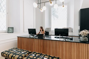 Welcome to our reception area, featuring a spacious desk with a laptop, telephone, and computer monitors, and a comfortable bench with a patterned cushion.