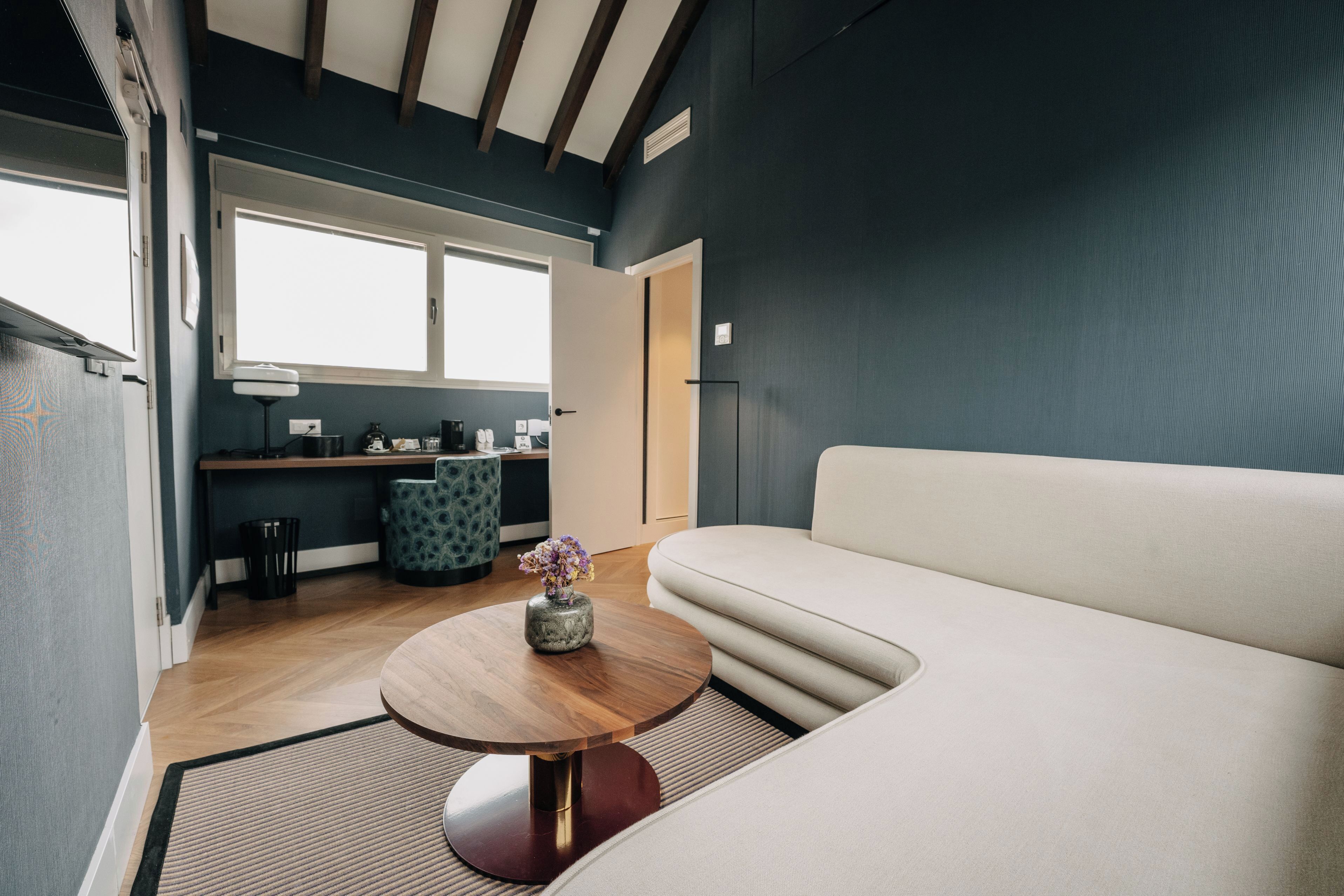 Una sala de estar moderna con un sofá, una mesa de centro de madera con un florero, y un área de cocina al fondo.