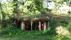 A rustic wooden structure with a thatched roof, surrounded by dense greenery and trees. - Le Nid dans les Bruyères (Fere-en-Tardenois)