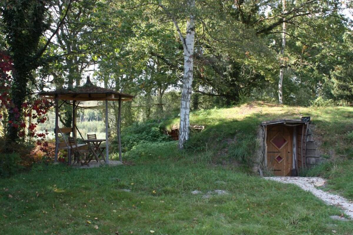 A gazebo with a table and chairs, a small wooden structure with a door, and a path leading to a hill.
