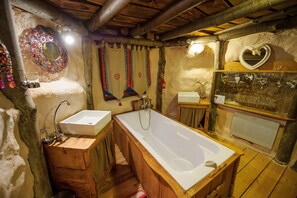 A rustic bathroom with a wooden vanity, a large bathtub, and a mirror with a decorative frame. - Le Nid dans les Bruyères (Fere-en-Tardenois)