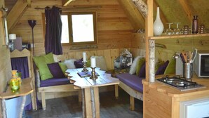 A cozy cabin interior with a wooden interior, a dining table, a sofa, and a kitchenette area. - Le Nid dans les Bruyères (Fere-en-Tardenois)