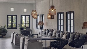 A modern living room with a sectional sofa, black woven chairs, and a coffee table. There are large windows with black frames and a textured wall. - Skiathos Blu (Skiathos)