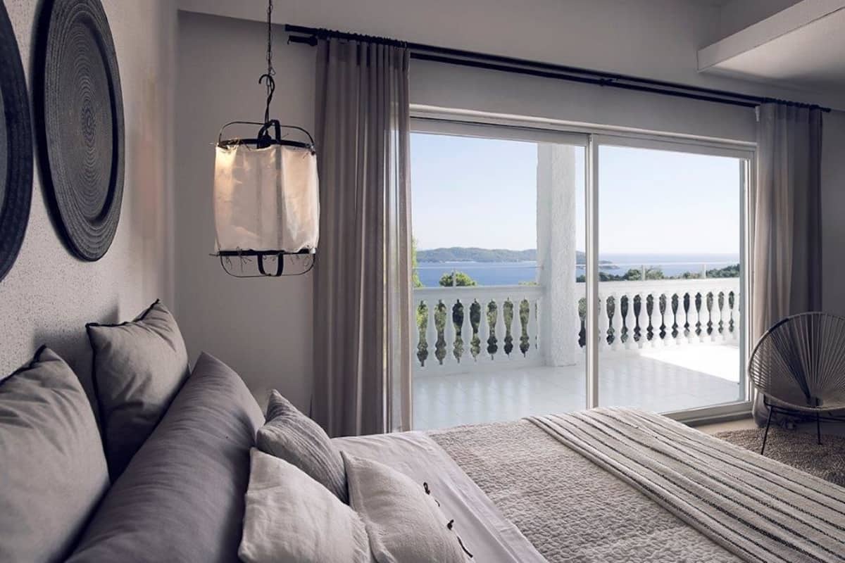 A bedroom with a large bed, a hanging light fixture, and a view of a balcony with a railing.